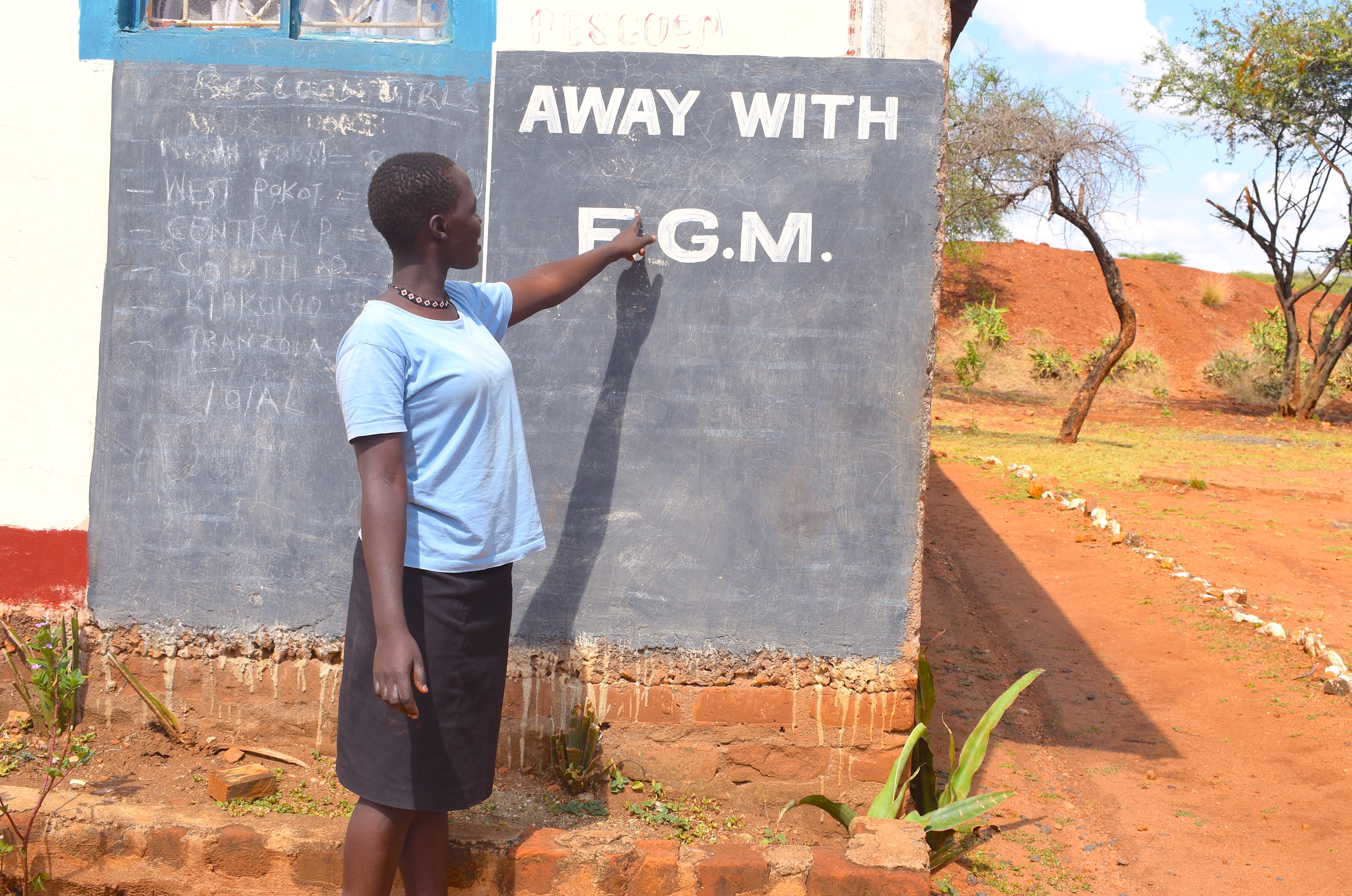A young girl pointing to a blackboard which says "Away with FGM"