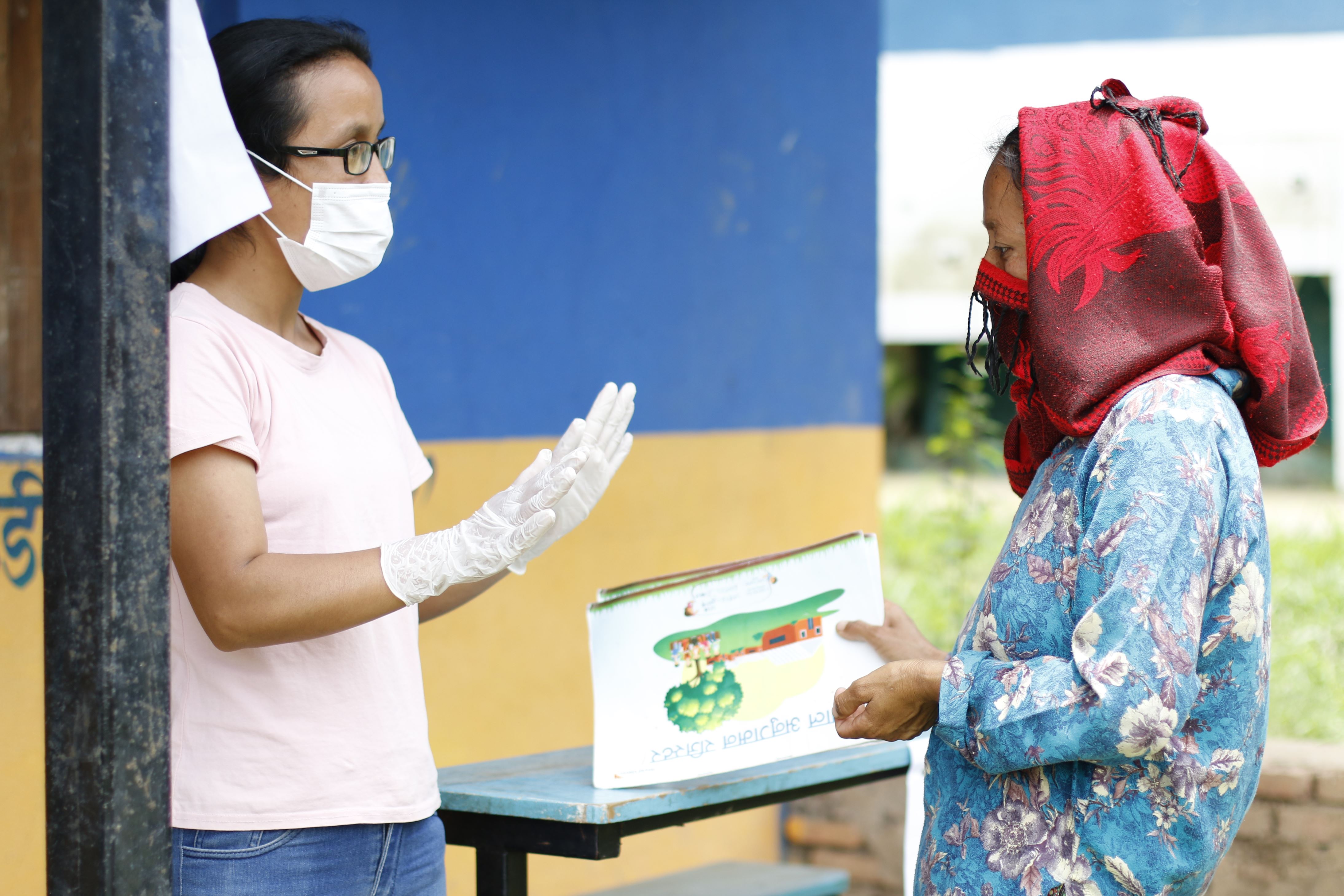 Two women from Nepal facing each other by the front of a blue and yellow building