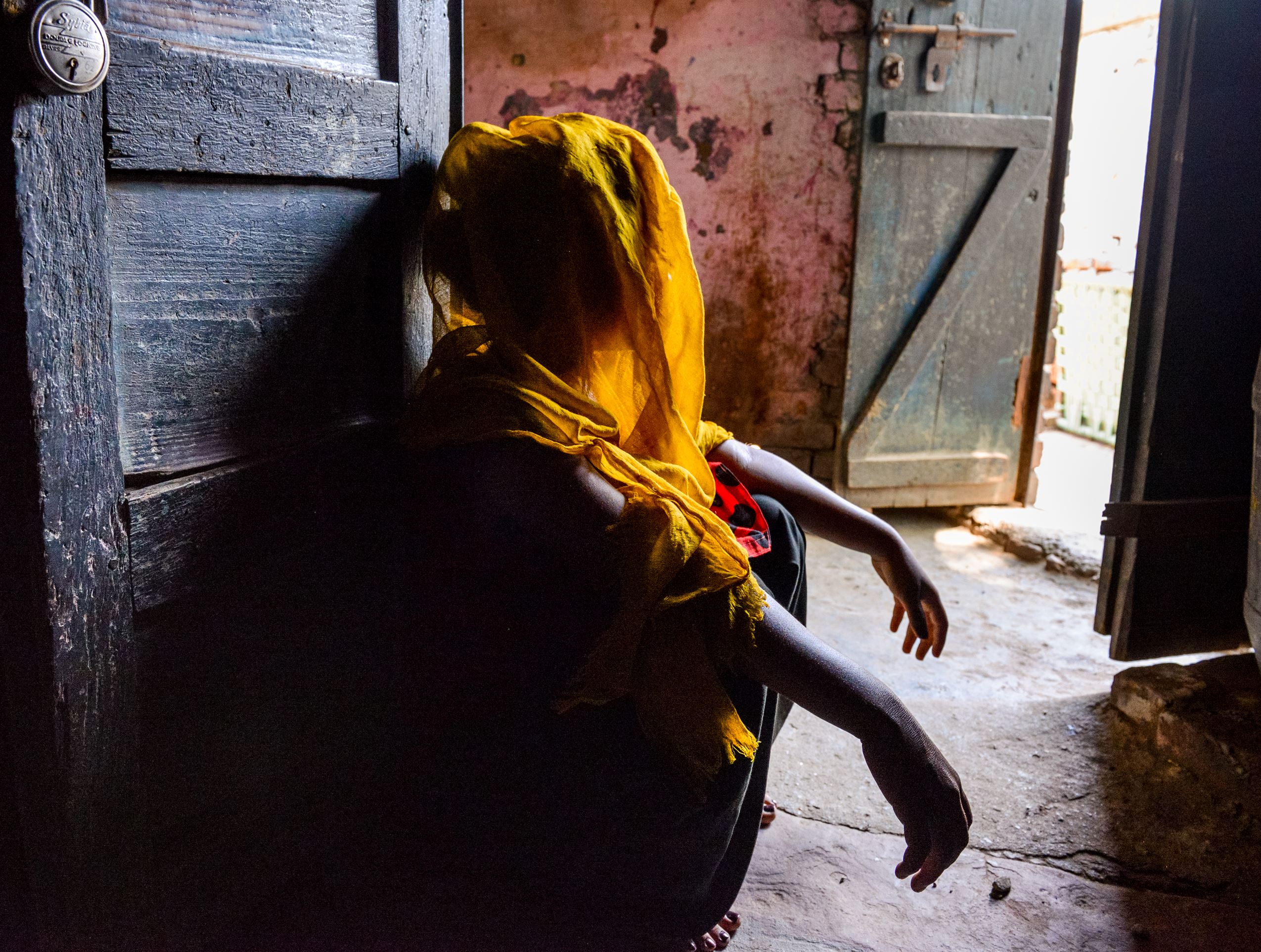 Girl in India looks away from the doorway, her face obscured, looking out of an open door