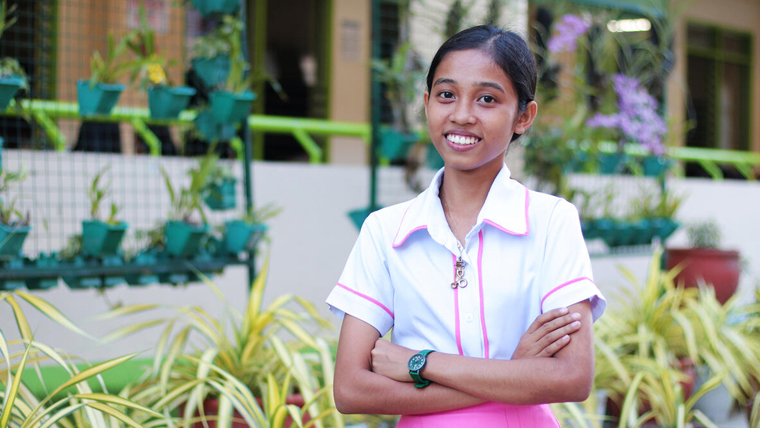 17-year-old Angel, in the Philippines, stands tall and smiles in front of hanging plants