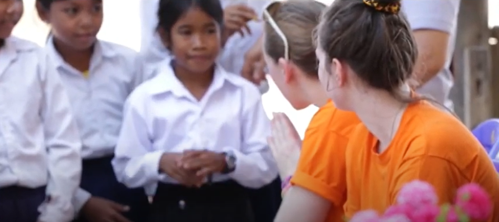 Two women in orange tops talk to children in school uniforms