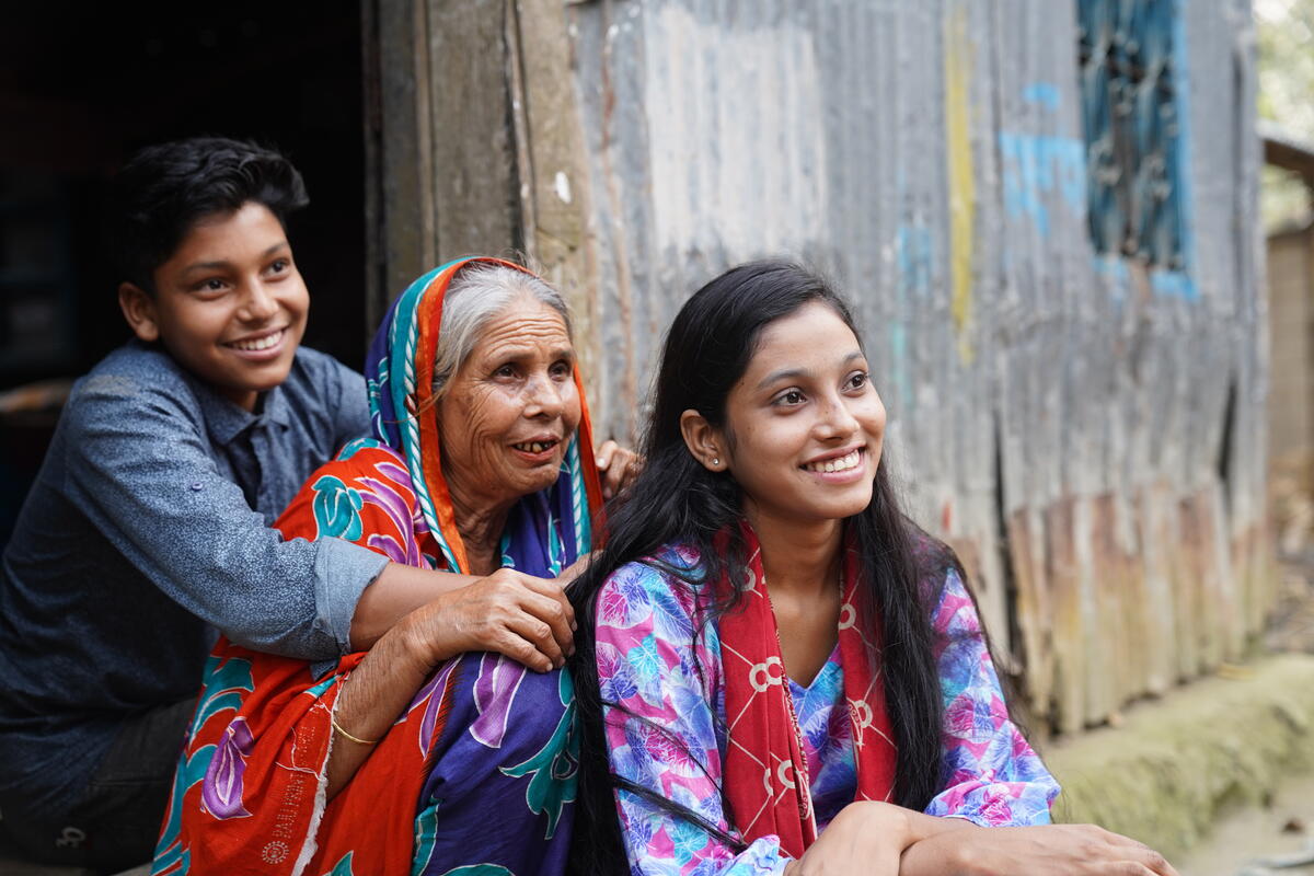 Bangladeshi teenage girl sits in front of her mother and brother.