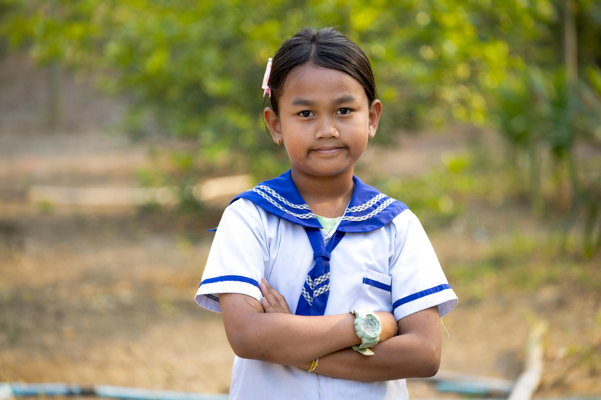 Rina in her school uniform looks at the camera and crosses her arms.
