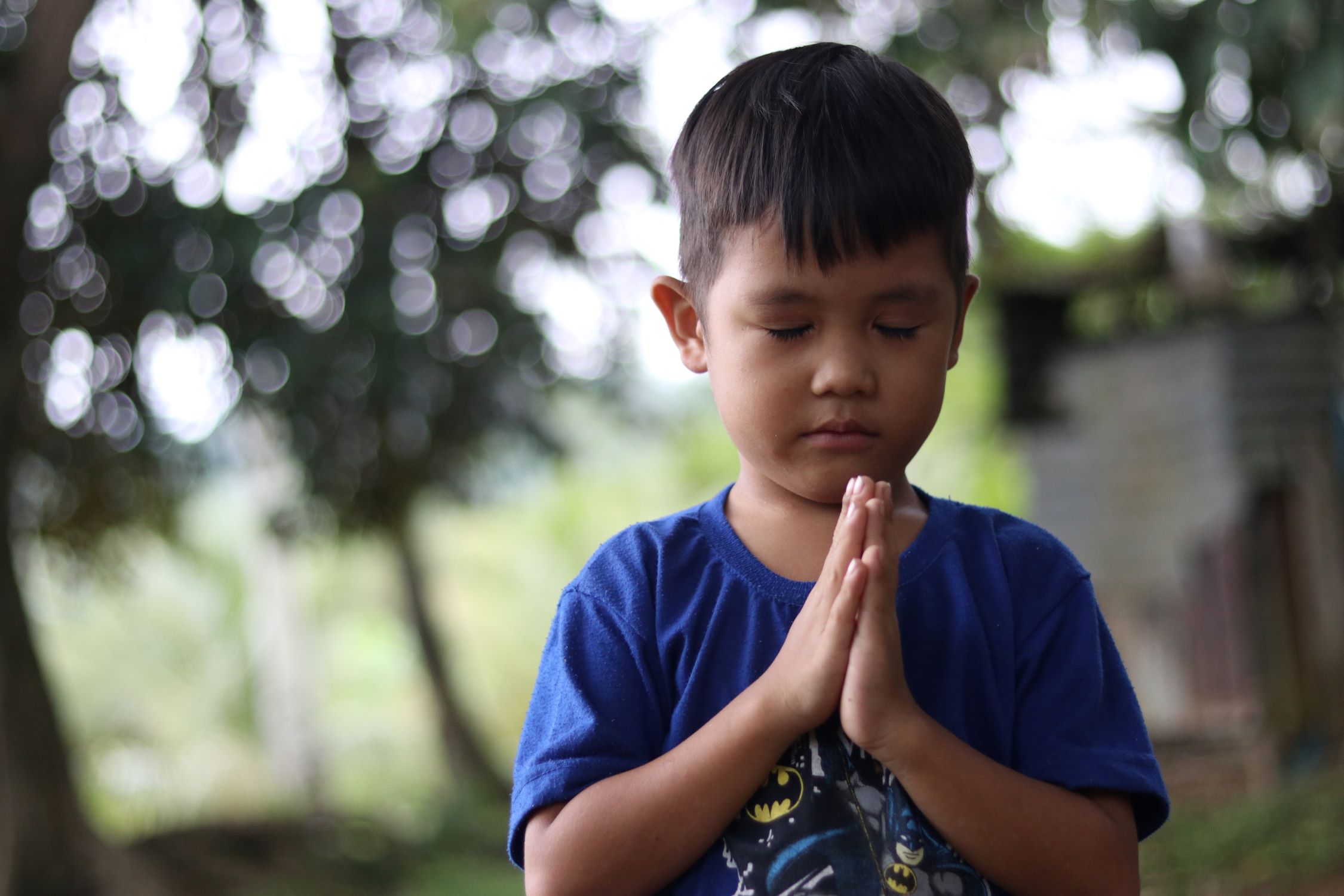 A young boy in the Philippines holds his hands together as if in prayer.