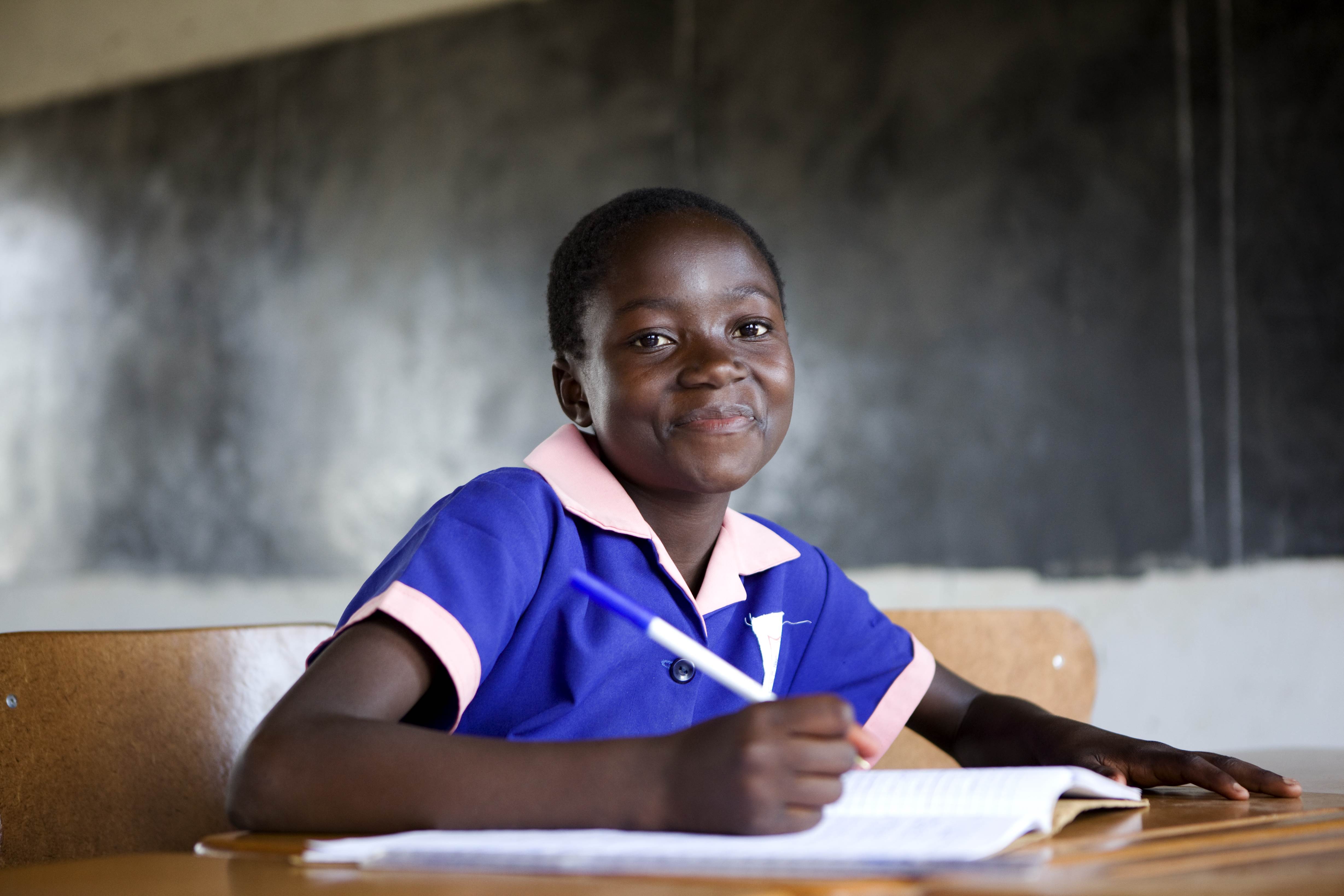 Girl in a blue school uniform at a desk looking and smiling to the camera