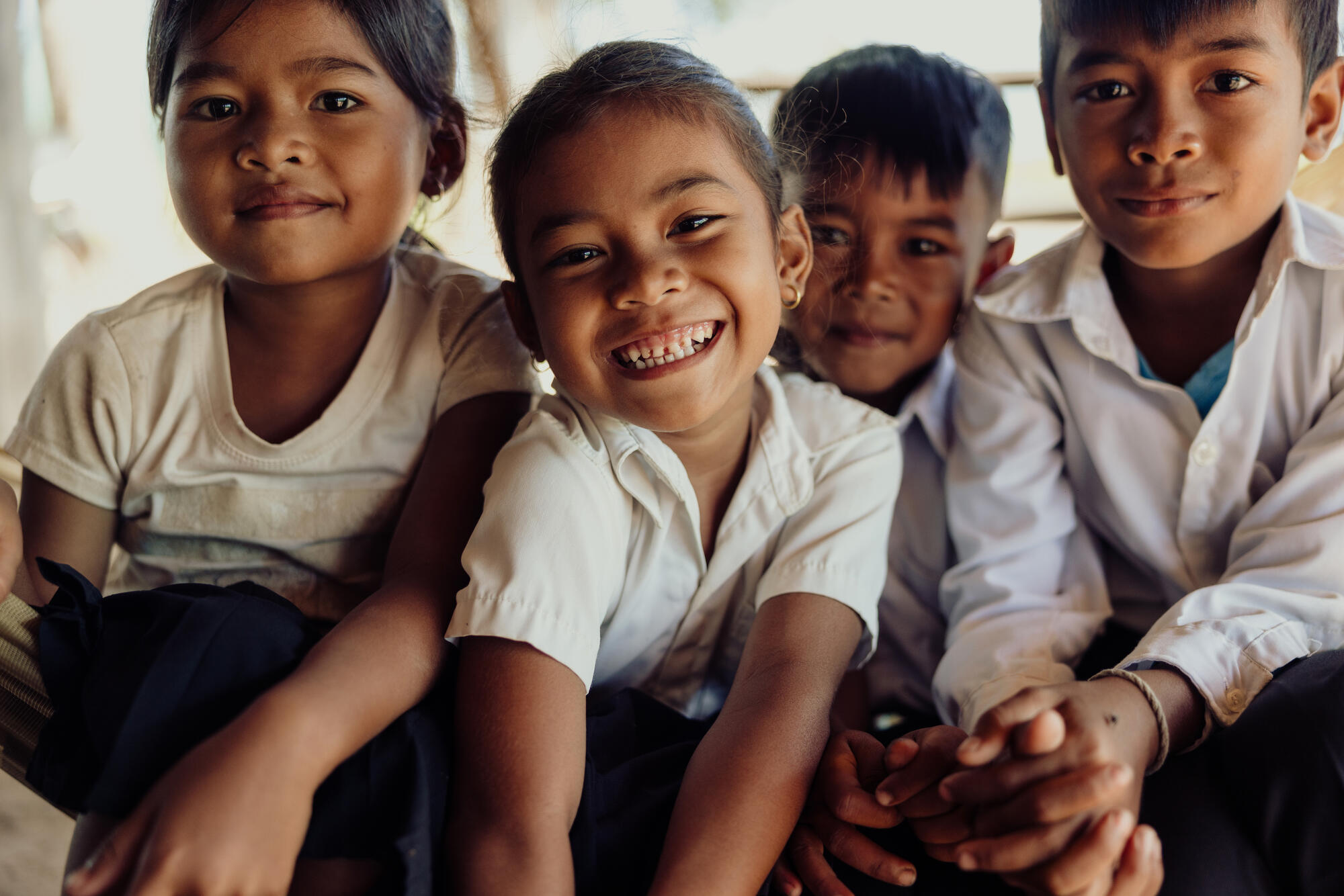 Two young girls and two young boys smile close up to the camera in Cambodia