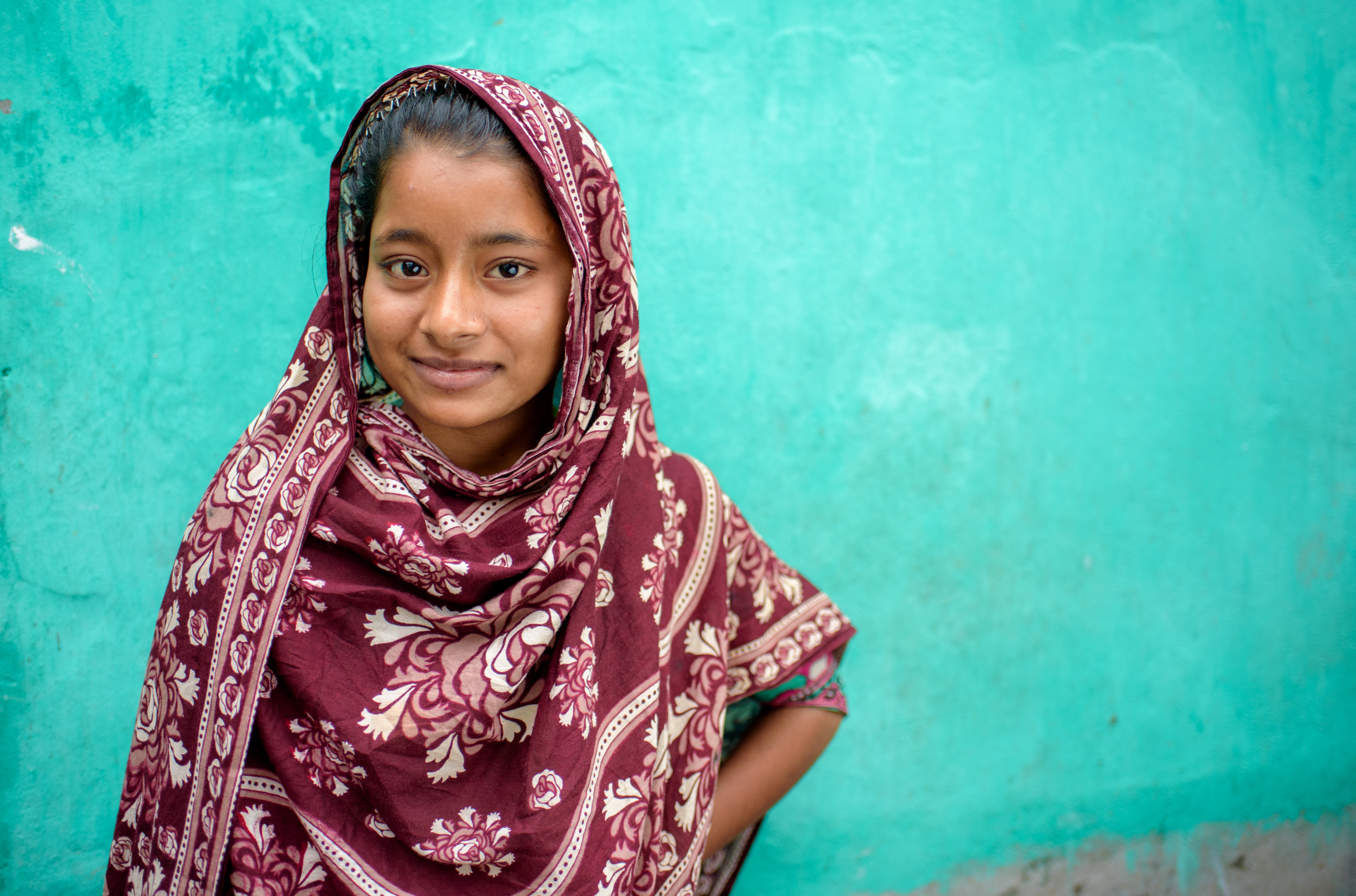 A girl from Bangladesh in a maroon sari with a teal wall background