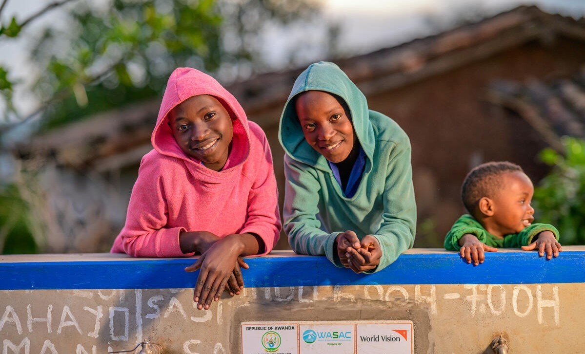 Two teenagers and a toddler pose by a newly installed water collection point