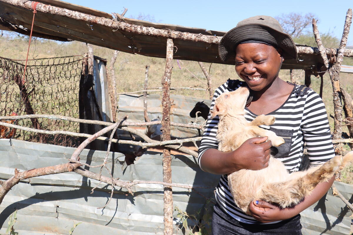 The recipient of two goats gifted via World Vision holding one of the goats and smiling.