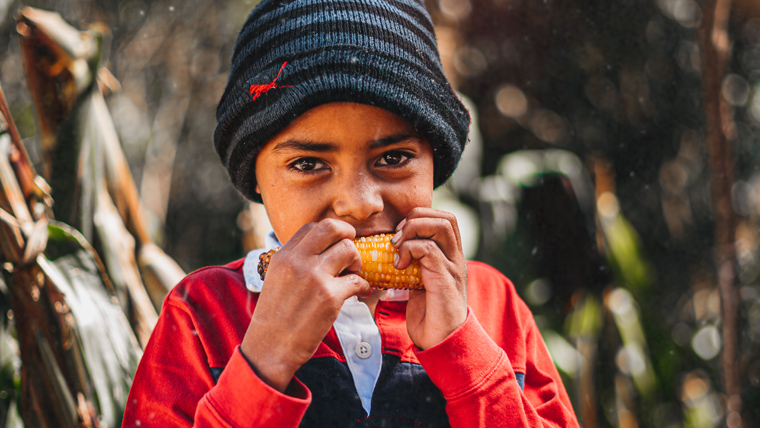 Victor eats a freshly cooked corn cob outside his mountain home