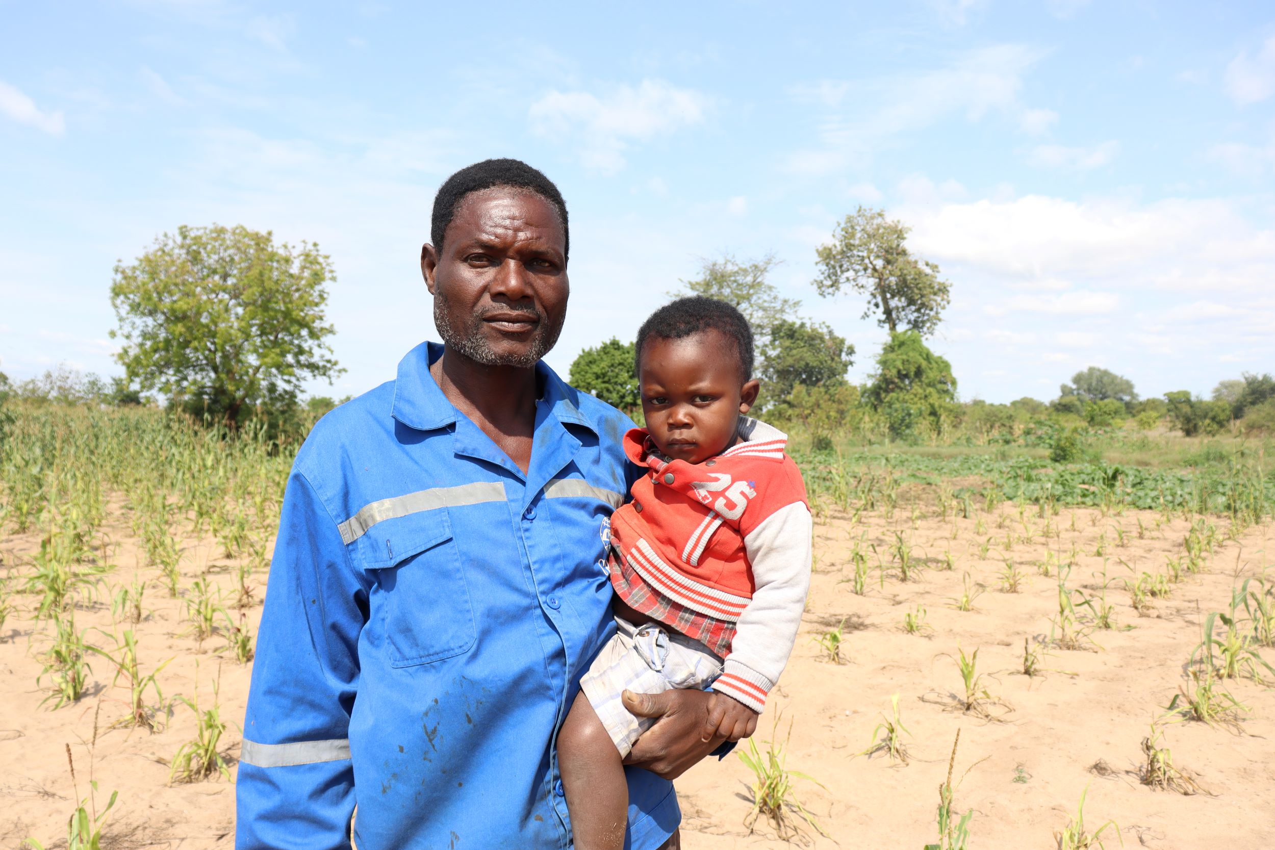 Farmer Fletcher poses in front of his field while holding his two year old grandson