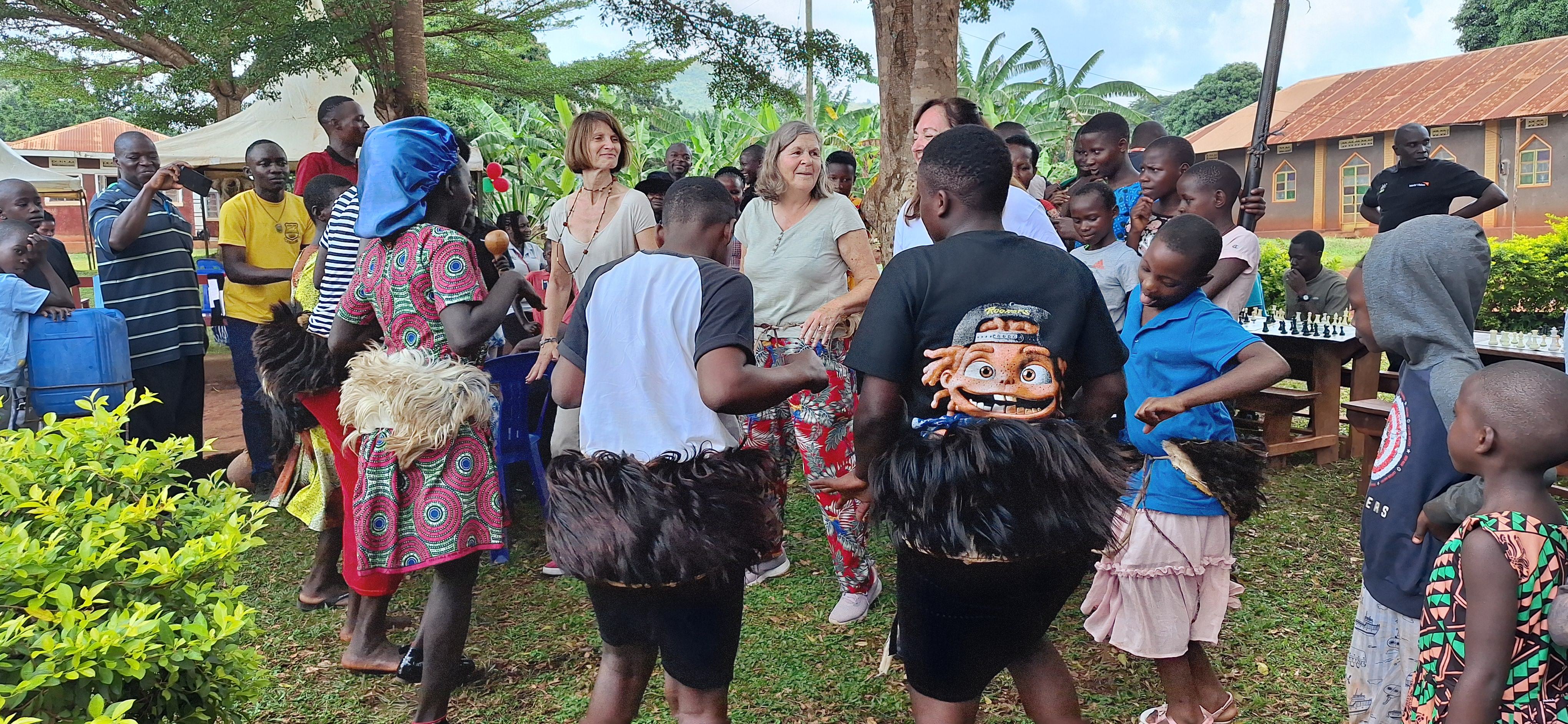 Emmanuelle is dancing with a group of locals in a circle, with others watching, taking photos or playing drums.