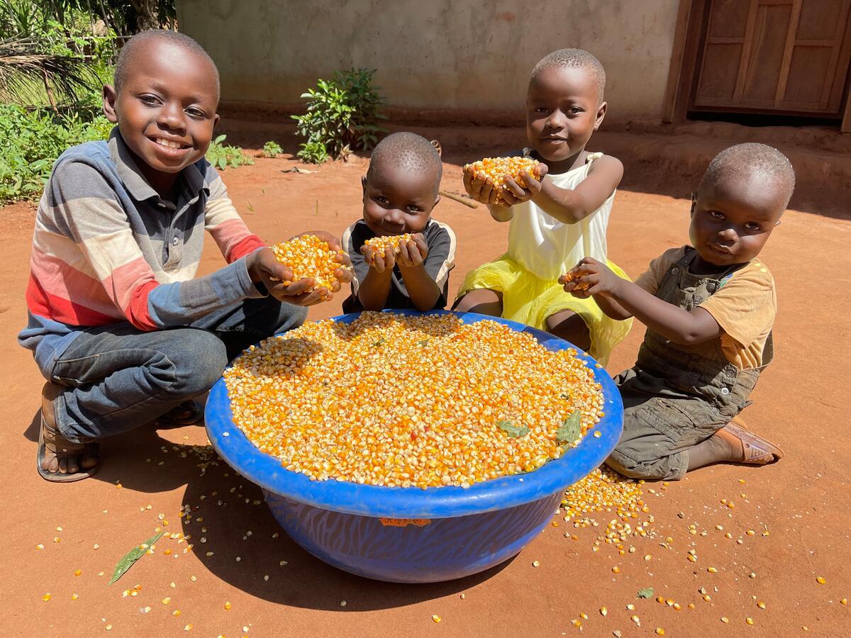 A group of young children in DRC hold up handfuls of maize from a large bowl in front of them
