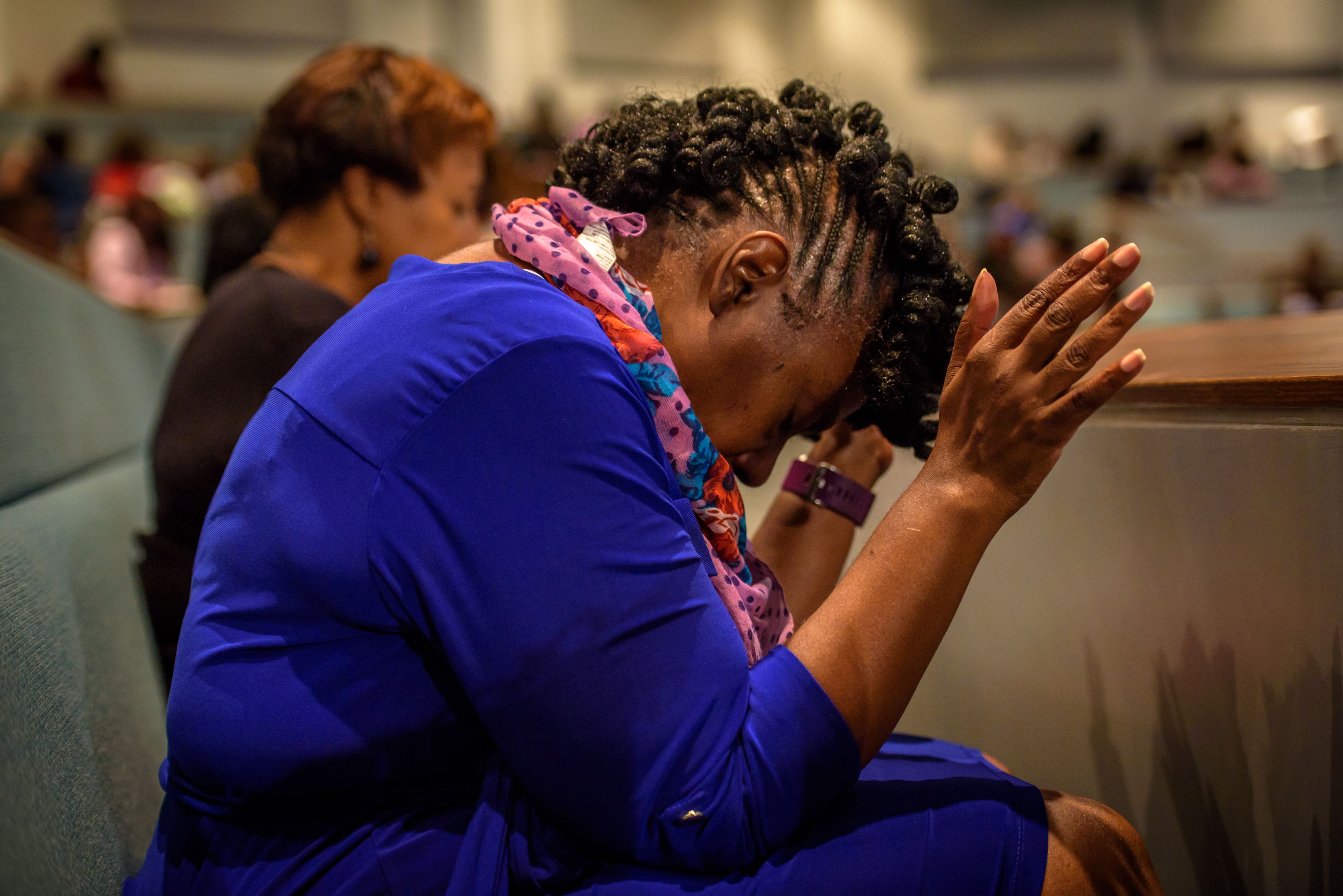Woman sits with her hands clasped, head bowed in prayer in a church in the US