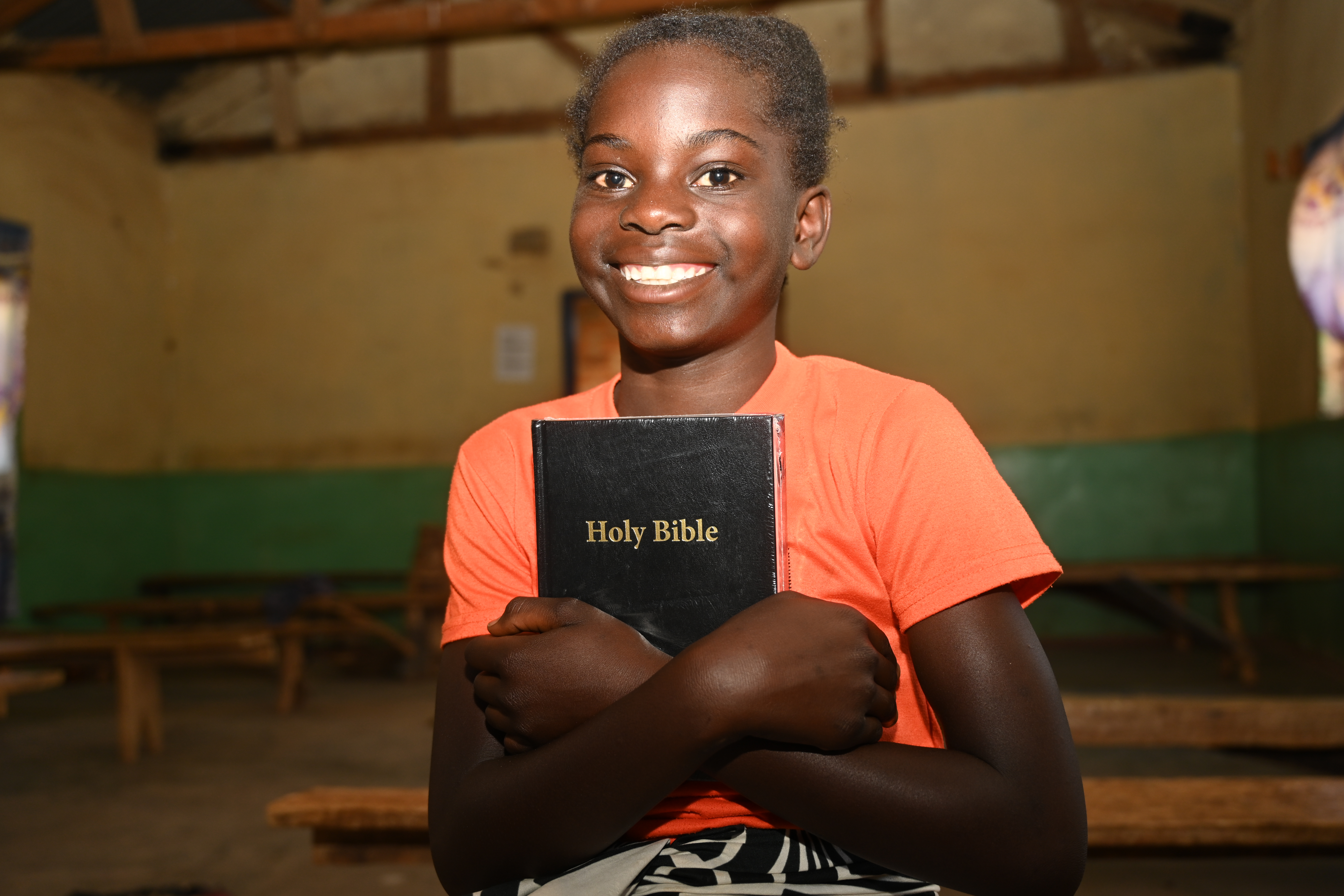 A young girl in Zambia smiles holding a copy of the Bible