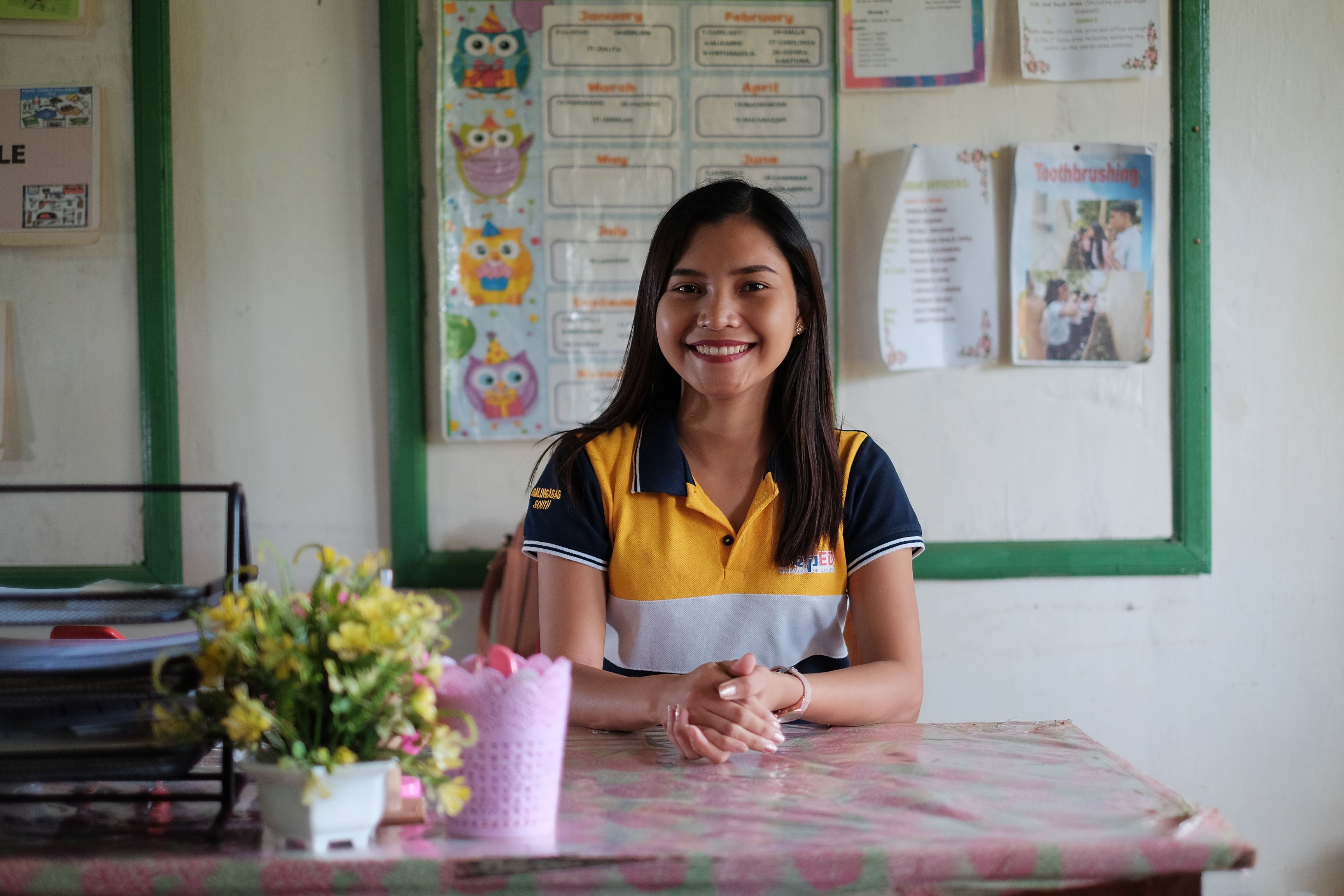 A young woman sits at a desk in the Philippines, ready to teach