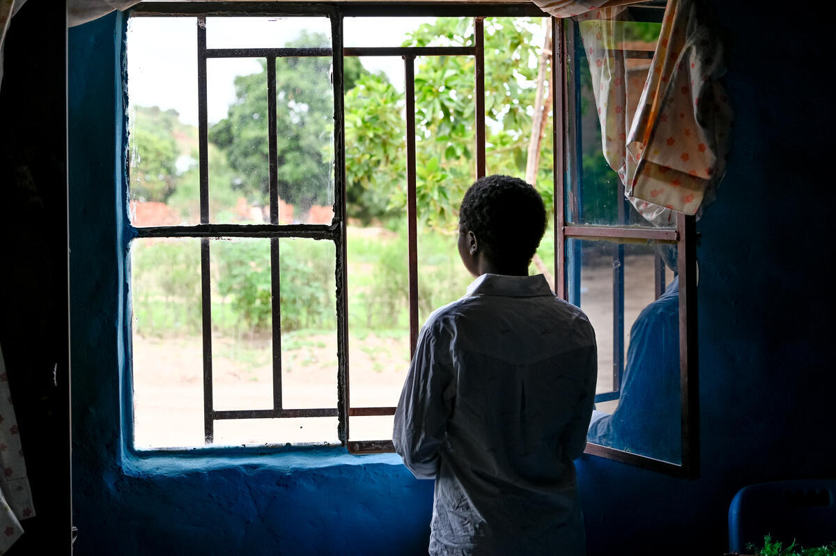 Young child from DRC seen from behind looking out of a window