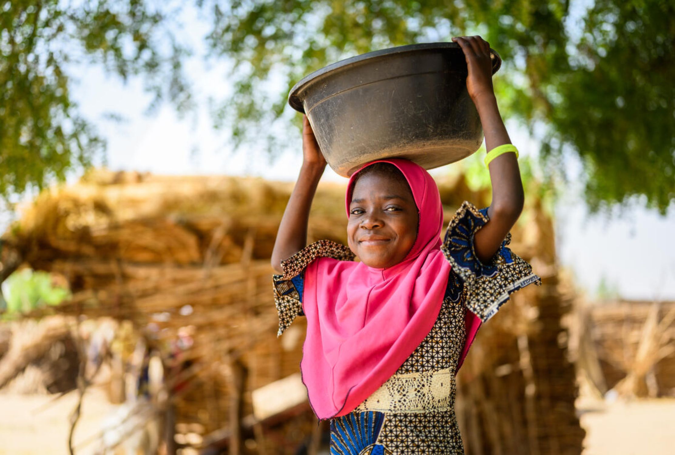 Girl smiles as she holds a basin for water above her head