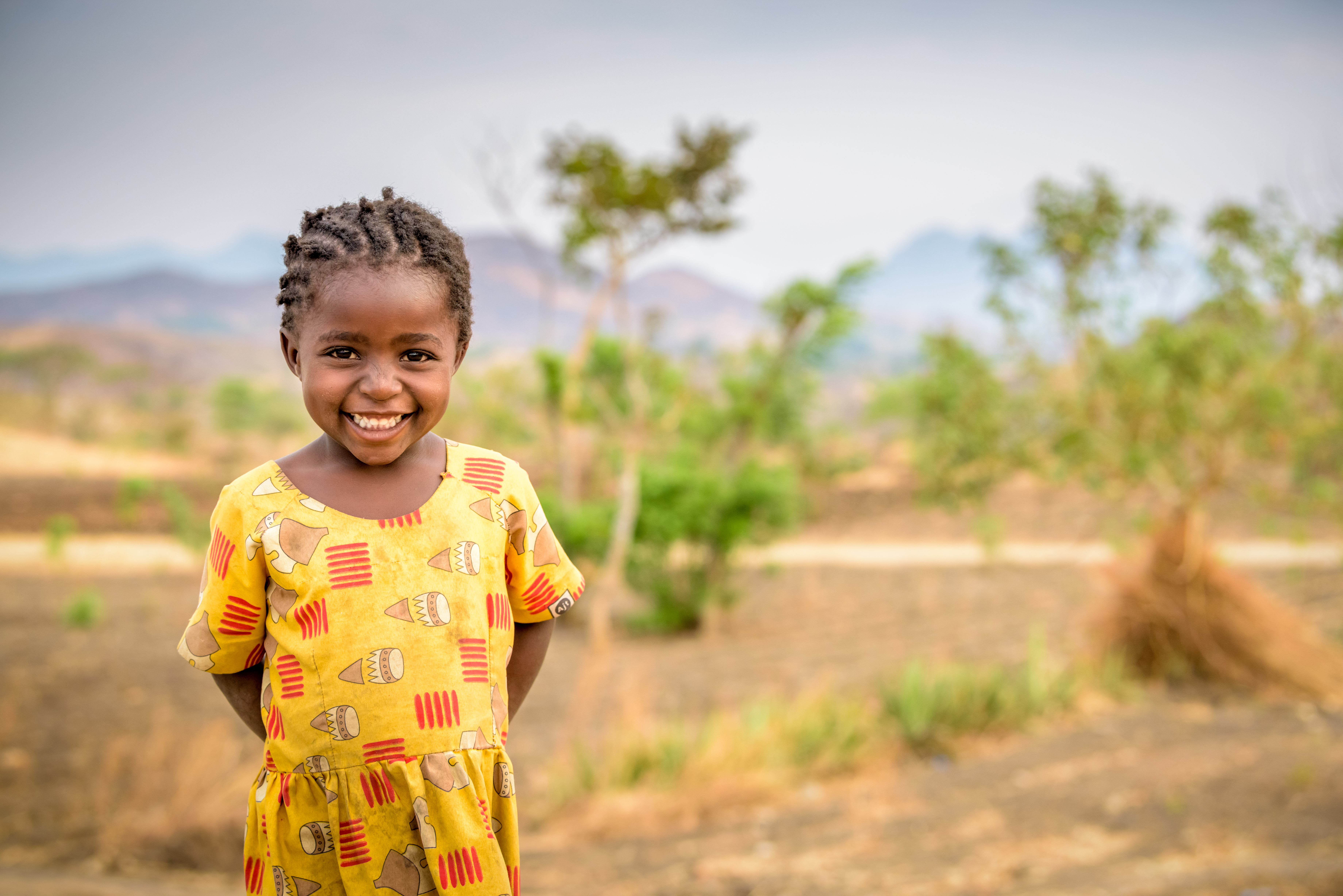Girl in Malawi smiles as she claps her hands behind her, standing in a green field