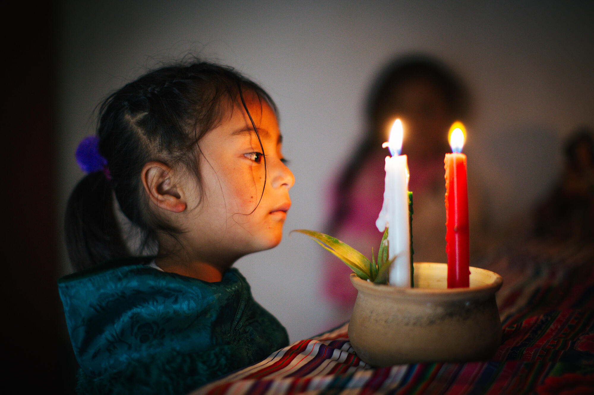 Young girl in Peru looks into a bowl in which two tall taper candles are burning, one red, the other whiteark