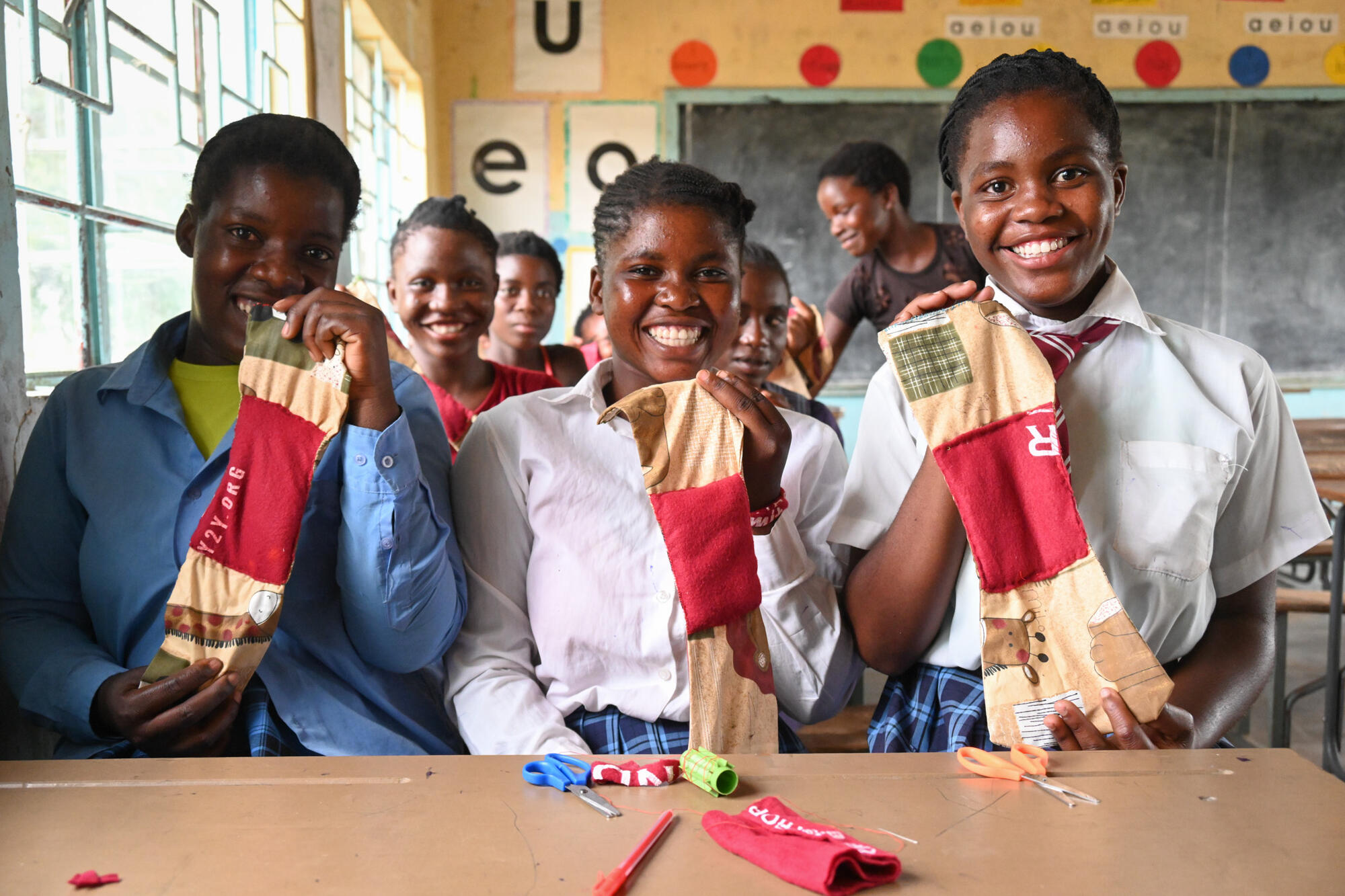 Three teenage girls hold up in class the reusable sanitary pads they've made in their class in Zambia.