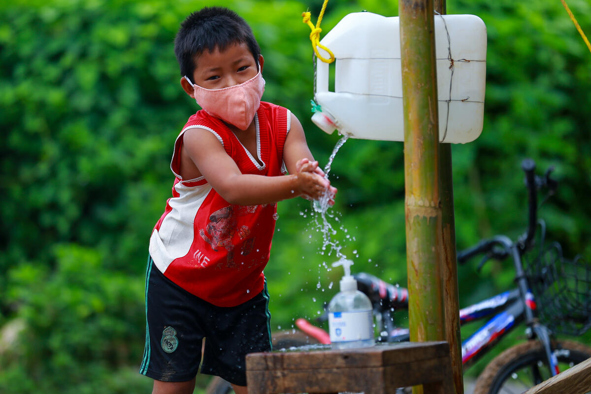 Boy in Myanmar holds hands out to wash them in water falling from a plastic bottle outdoors