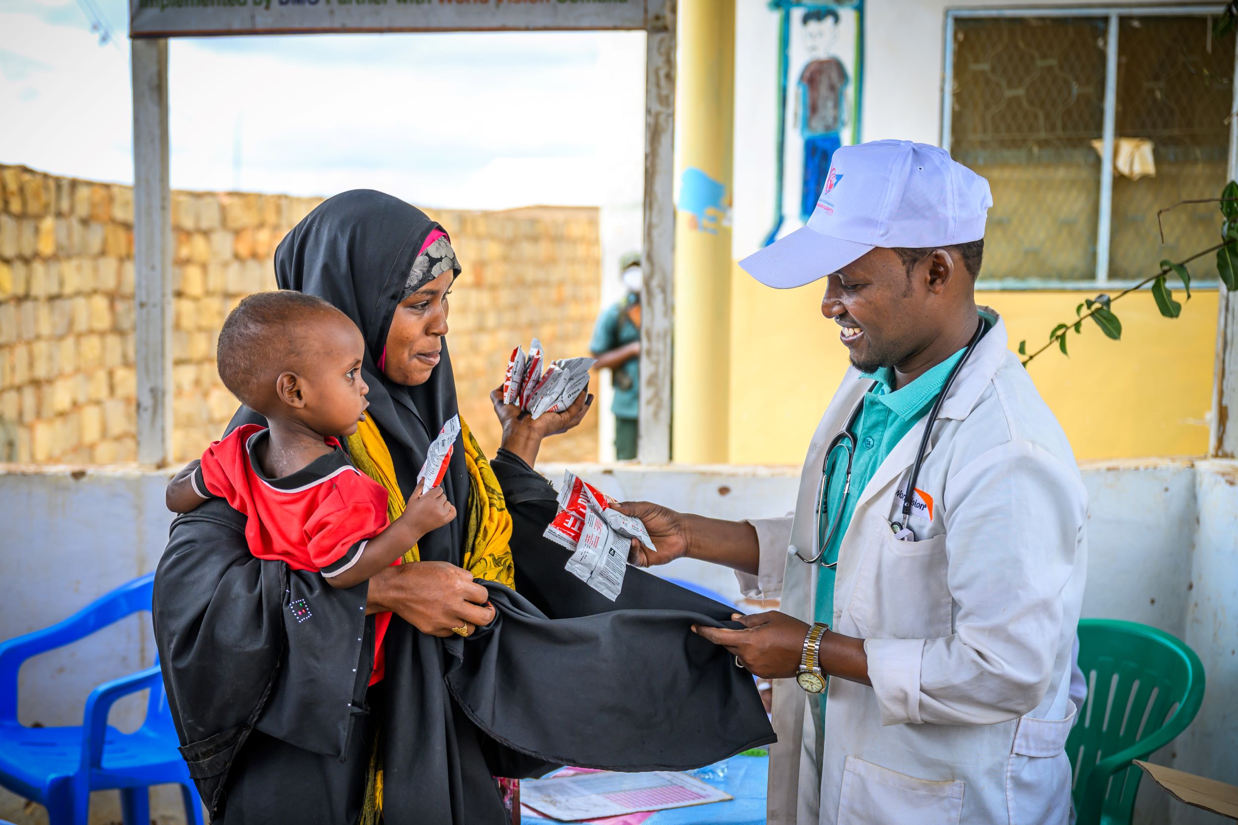 Muad, one, carried by his mother, receives ready-to-use therapeutic food from a health worker