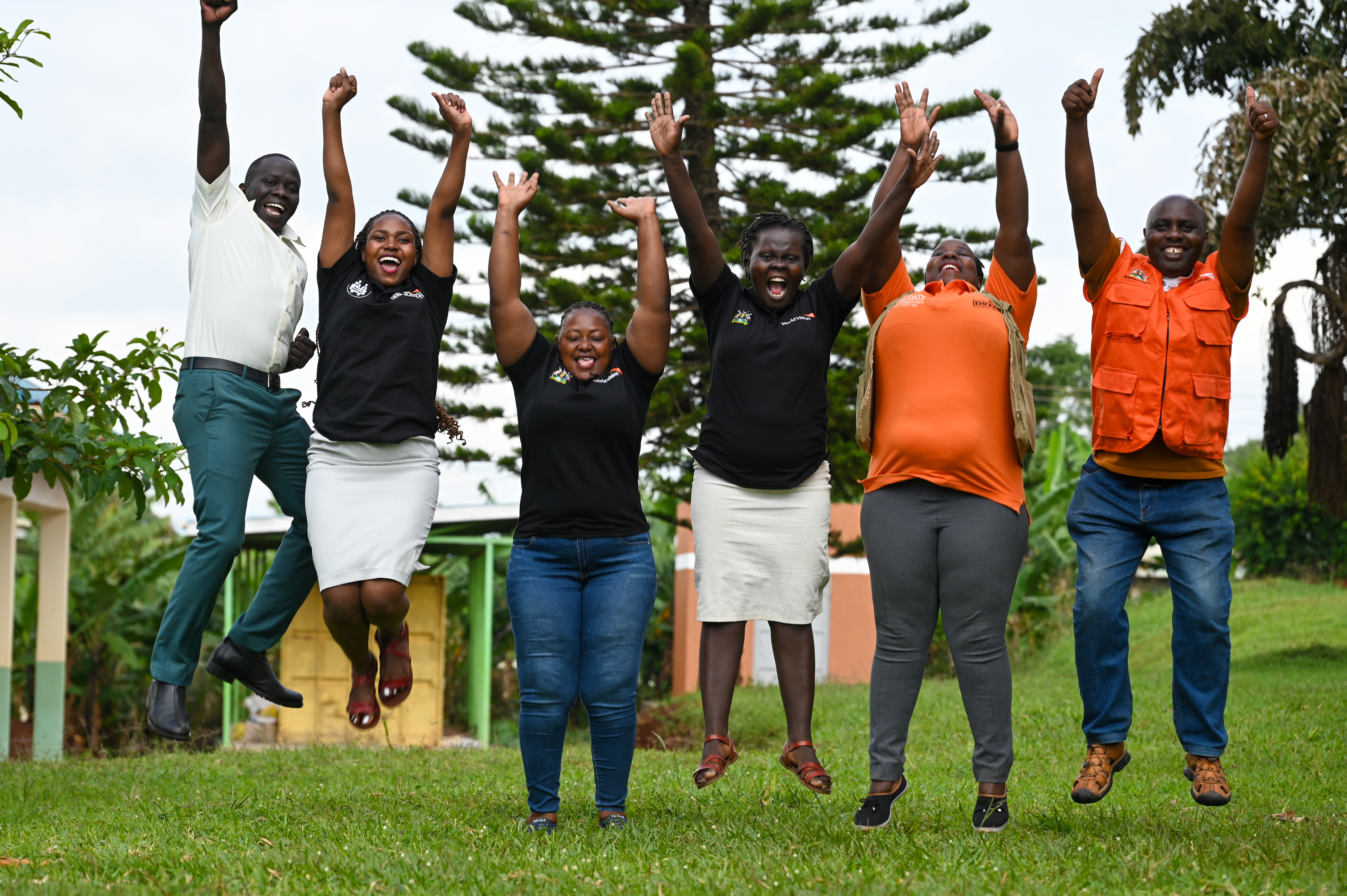 Male and female members of the local World Vision team jump in the air with arms stretched and big smiles