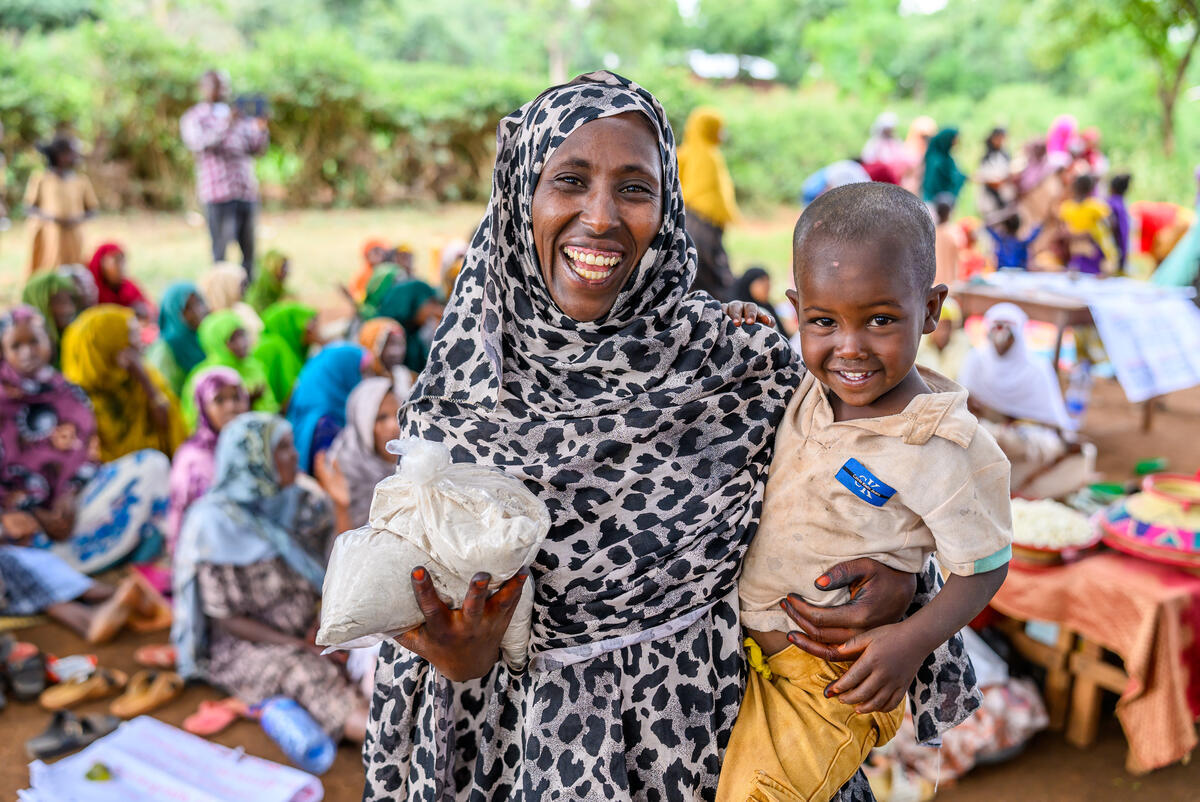 Mother and toddler smiling, holding food supplies.