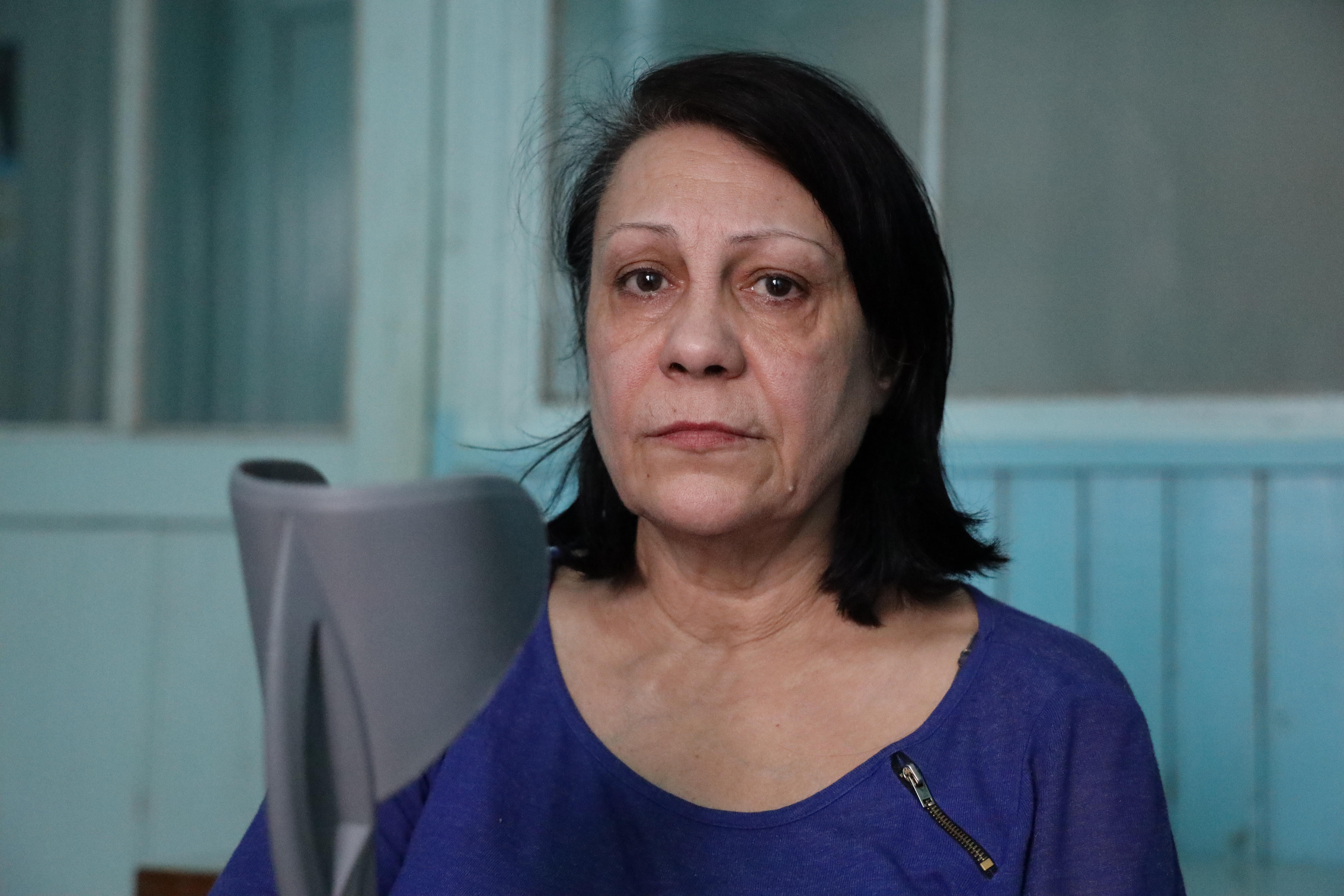 A woman in purple sits holding her crutches and looks directly into the camera