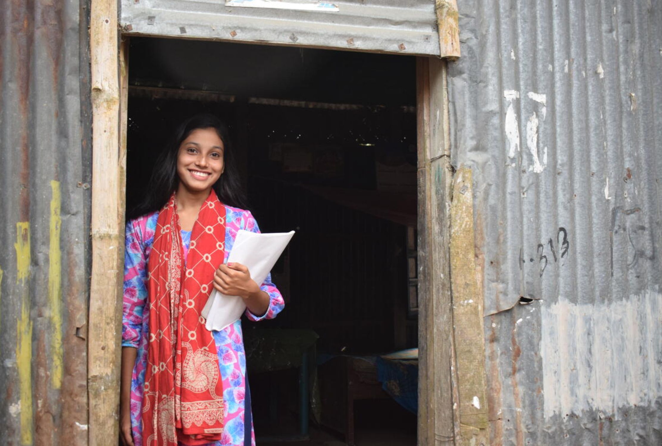 A girl standing in a doorway and smiling now she has escaped child marriage thank to World Vision